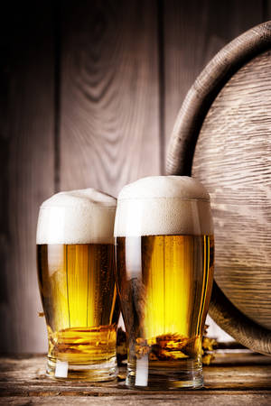 Two glass of light beer on background of wooden barrelsの写真素材