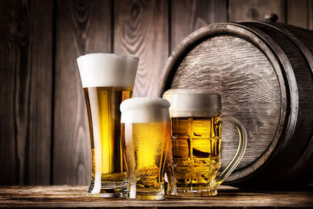 Two glasses and mug of light beer on a background of the old wooden barrelsの写真素材
