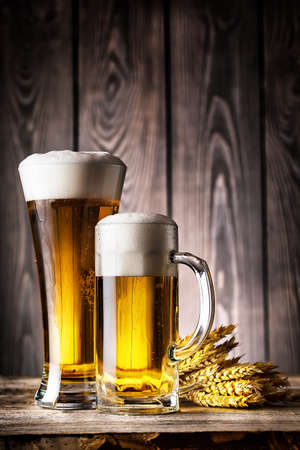 Glass and a mug of light beer with foam and ears on the wooden backgroundの写真素材