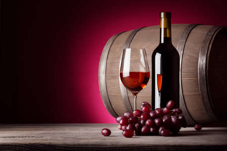 Glass of red wine with bottle and grapes on red backgroundの写真素材