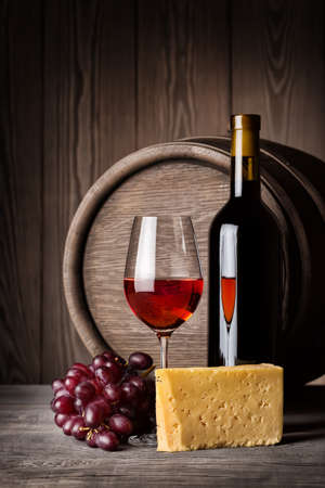 Glass of red wine and cheese with a bottle on the background of wooden wallの写真素材