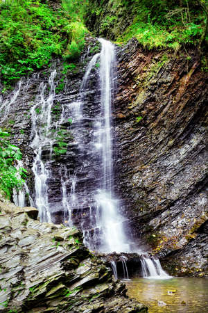Falls among the black rocks in the green forestの写真素材
