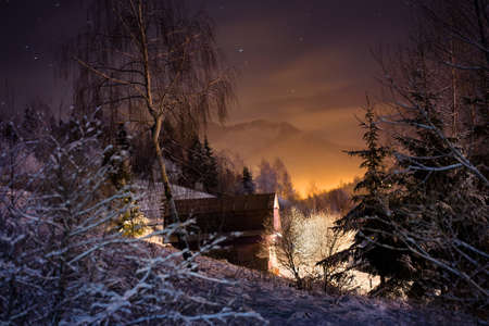 Illuminated house in winter forest in the mountainsの写真素材