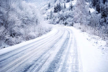 Snow-covered road in forest between mountainsの写真素材