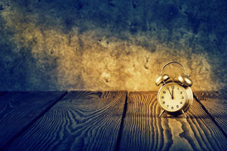 Old alarm clock under beam of light on wooden table