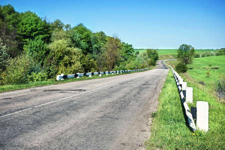 Asphalt road broken in field with green grassの写真素材