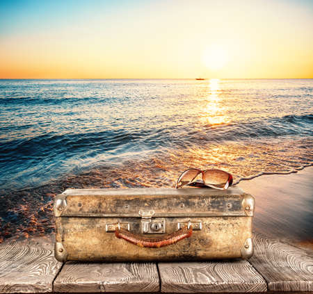 Suitcase with sunglasses on wooden pier on background of sea sunsetの写真素材