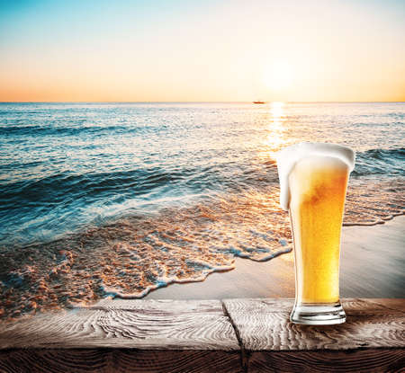 Glass of beer with foam on a table against the seaの写真素材
