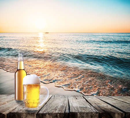 Mug and bottle of beer on a table against the seaの写真素材