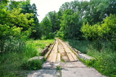 Wooden bridge over the river overgrown with grass in the summerの写真素材