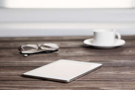 Tablet computer and a cup on a wooden table