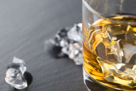 Detail of a glass of whiskey and ice cubes shot with selective focus on the dark backgroundの写真素材
