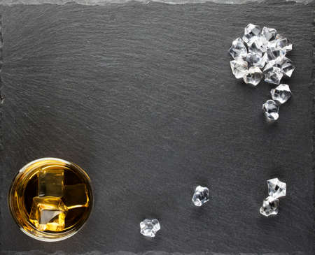 Round glass of whiskey and ice cubes scatteredの写真素材