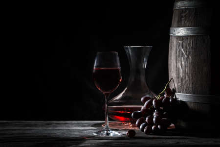 Glass of red wine, decanter and a barrel on dark backgroundの写真素材