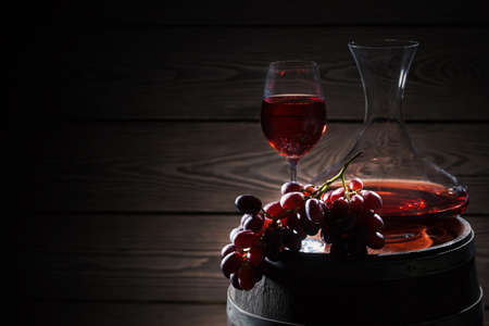 Red wine and a bunch of grapes on a wooden barrelの写真素材
