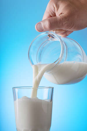 Hand pouring milk from a jug into a glass on a blue background. The concept of healthy natural food.の写真素材