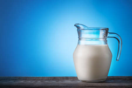 Jug with milk on a wooden table with a blue backgroundの写真素材