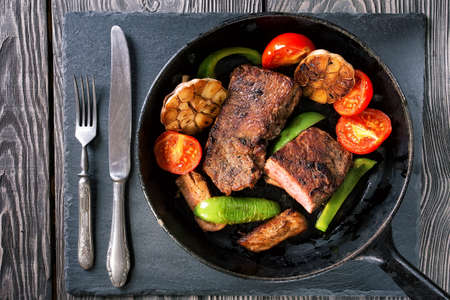 Frying pan with steak and vegetables on the tableの写真素材