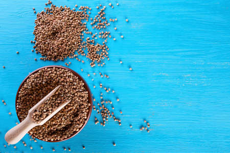 Clay bowl with buckwheat and a wooden spatula on a blue background. View from above. The concept of...