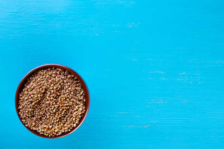 Clay brown bowl with raw buckwheat on blue backgroundの写真素材