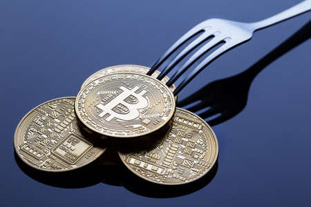 Bitcoin fork. The concept of the division of the crypto currency. Golden bitcoins with a fork on a blue business background.の写真素材
