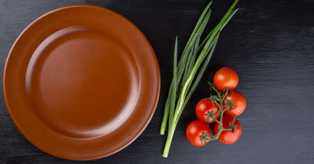 Brown clay dish and tomatoess on black backgroundの写真素材
