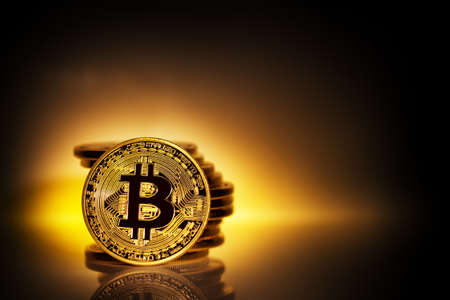 Gold bitcoin on yellow background with pile of coinsの写真素材