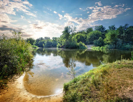 Sandy bay on the lake with green trees on shoreの写真素材