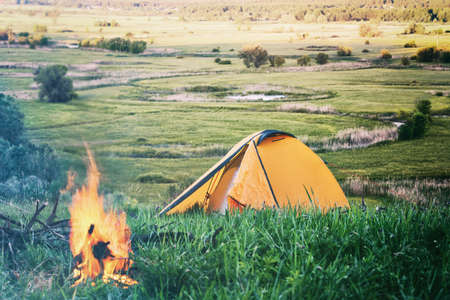 Orange tent with fire in field with green grassの写真素材