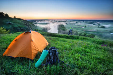 Orange tent and backpack on hill with touristの写真素材