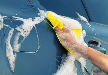 Washing the gray car with yellow rag in soapy foamの写真素材