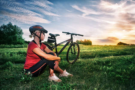 A girl in bicycle helmet sits near bicycleの写真素材
