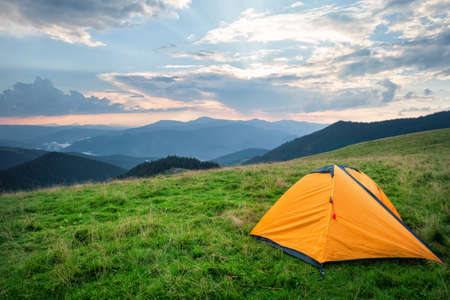 Orange tent on green grass in mountains in summerの写真素材