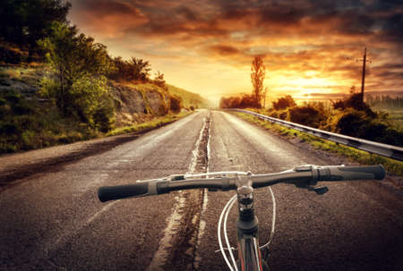 Bicycle wheel on the background of the old asphalt road under the sunset skyの写真素材