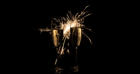 Two tall glasses of champagne in bright sparks on a black backgroundの写真素材