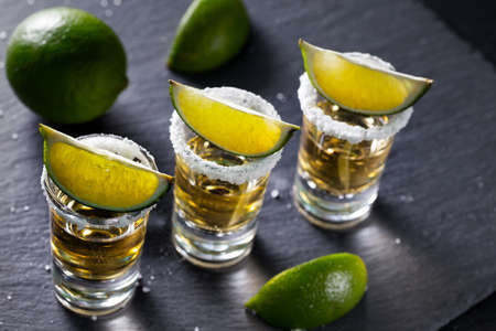 Three piles of mexican golden tequila with lime and salt on a black backgroundの写真素材