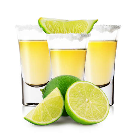 Three glasses of golden tequila with whole and sliced limeの写真素材