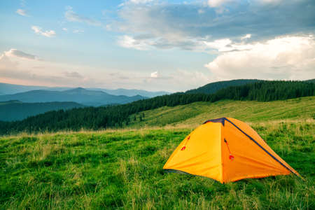 Orange tourist tent in green mountainsの写真素材