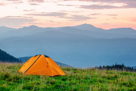 Orange tent on meadow in mountains under pink skyの写真素材