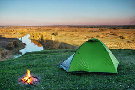 Green tourist tent in green grass of hill above riverの写真素材