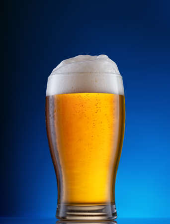 Light beer with white foam in glass on blue backgroundの写真素材