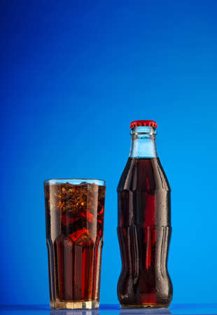 Glass of brown carbonated drink and bottle on blue backgroundの写真素材