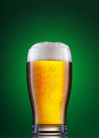 Glass of light beer with foam on the green backgroundの写真素材