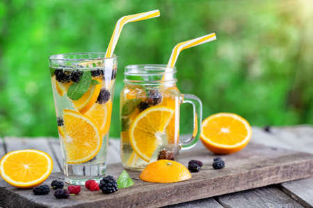 Glass and jar of lemonade cocktail with orange slices and berriesの写真素材