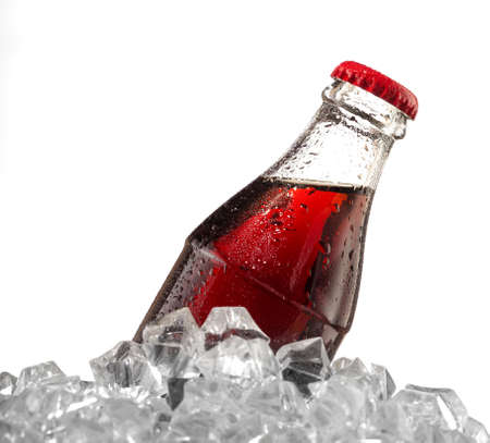 Brown carbonated drink in wet bottle with red cap in ice cubesの写真素材