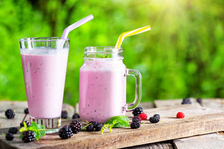 Berry smoothie in jar and glass under bright sunの写真素材