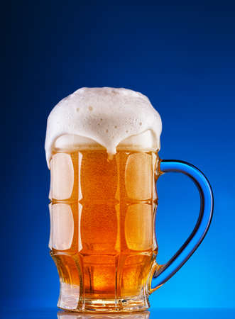 Faceted mug of the light beer with foam on blue backgroundの写真素材