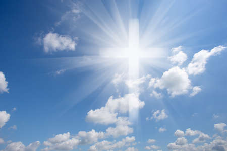 Christian shining cross in the blue cloudy sky. Symbol of faith and paradise. Conceptual collage.の写真素材