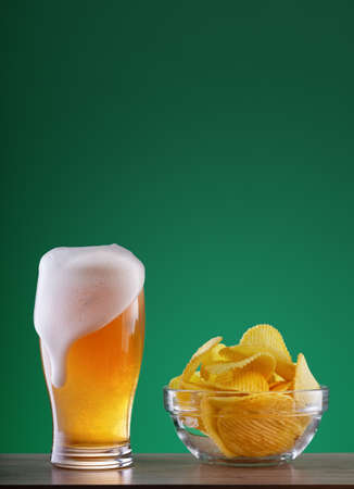Glass of light beer with drip foam and plate of chipsの写真素材
