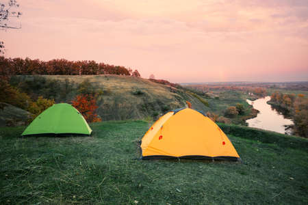 Camping from orange and green tents on banks of riverの写真素材